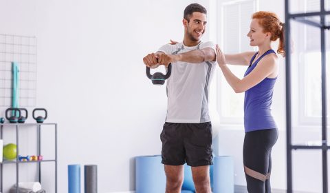 Smiling personal trainer and sportswoman working out with weight at gym